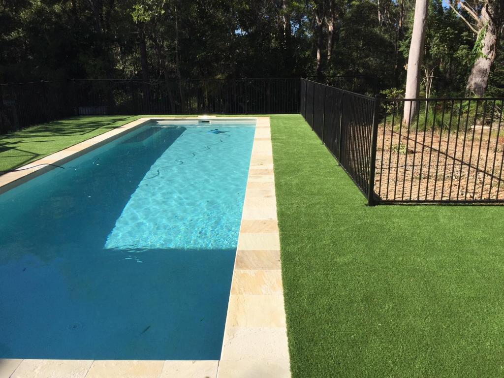 a blue swimming pool with green grass next to a fence at Eatons Retreat in Eatons Hill