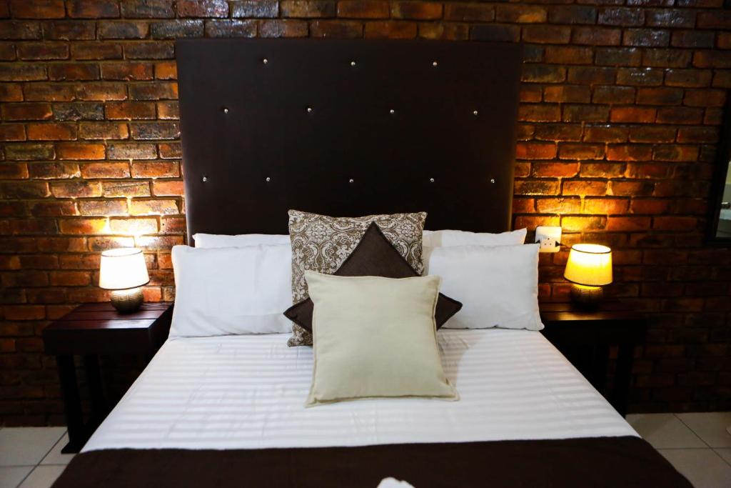 a bedroom with a large white bed with a brick wall at Gracious Lodge in Burgersfort