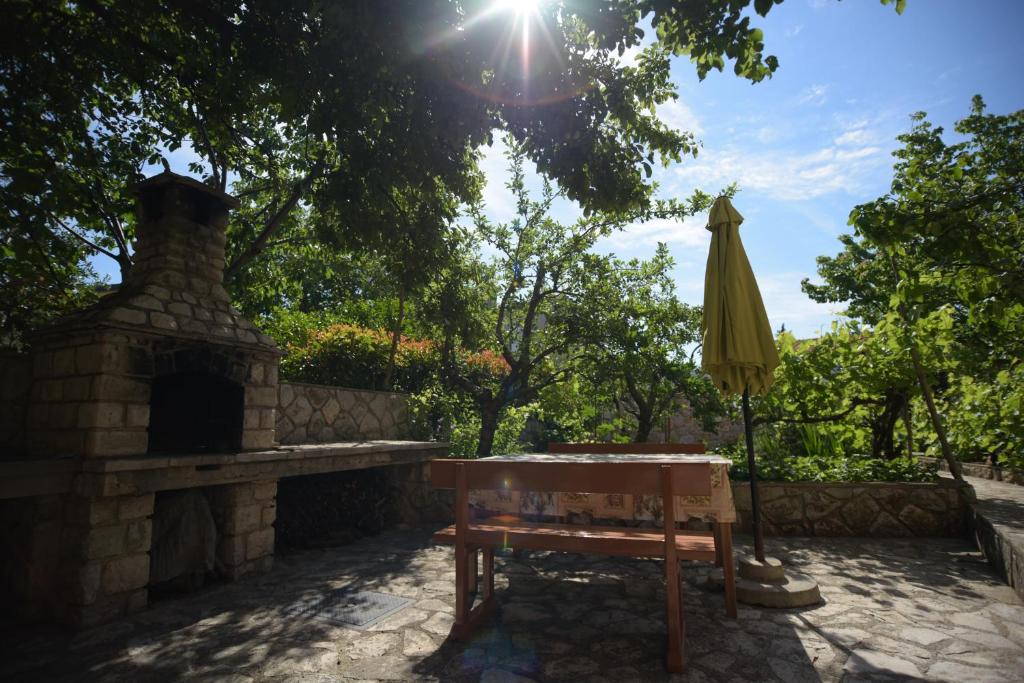 an umbrella and a bench next to a stone fireplace at Apartmani Vitković II Cres in Cres