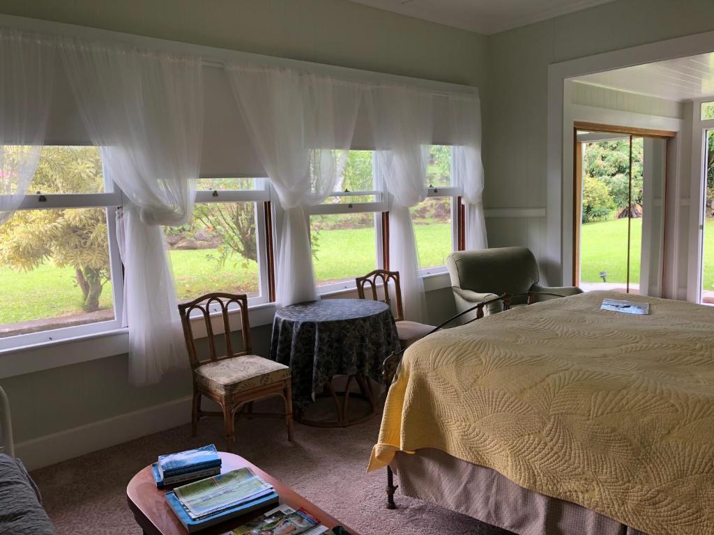 a bedroom with a bed and two chairs and windows at Old Hawaiian Bed and Breakfast in Hilo