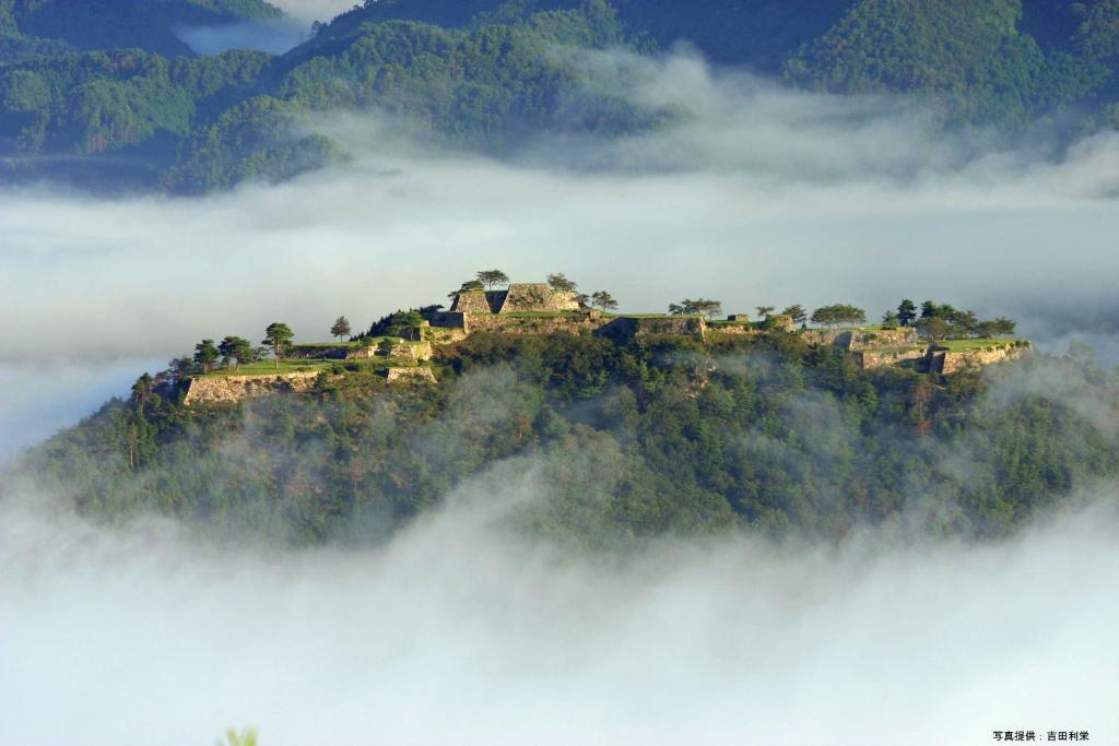 a mountain in the clouds with a house on it at Gunkakutei in Asago