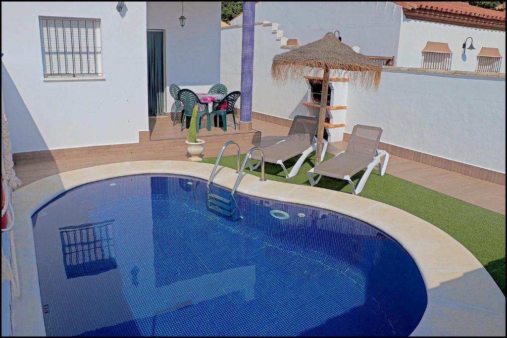 a swimming pool in a yard with chairs and a house at Chalet Muelle Pesquero 65 in Conil de la Frontera