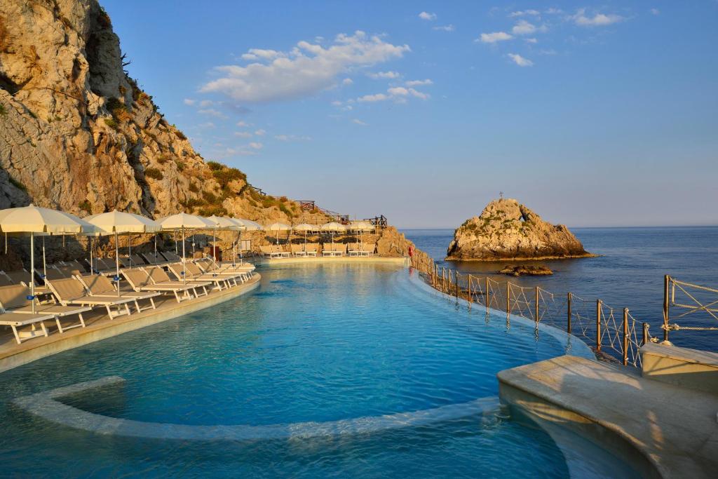 a swimming pool next to the ocean with tables and chairs at UNA HOTELS Capotaormina in Taormina