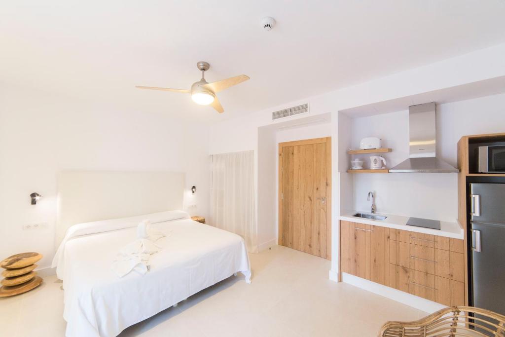 a white bedroom with a bed and a kitchen at Sa Cala Suites in Es Calo