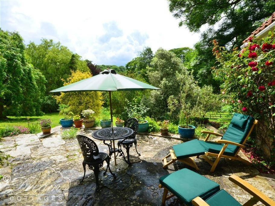 un patio con mesa, sillas y sombrilla en Sixpenny Cottage, en Upwey