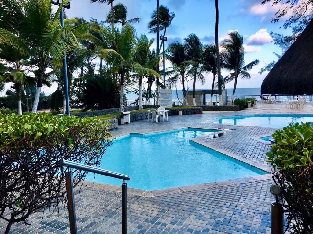 una piscina con palmeras y el océano en Suite Golden Beach Frente Mar, en Recife