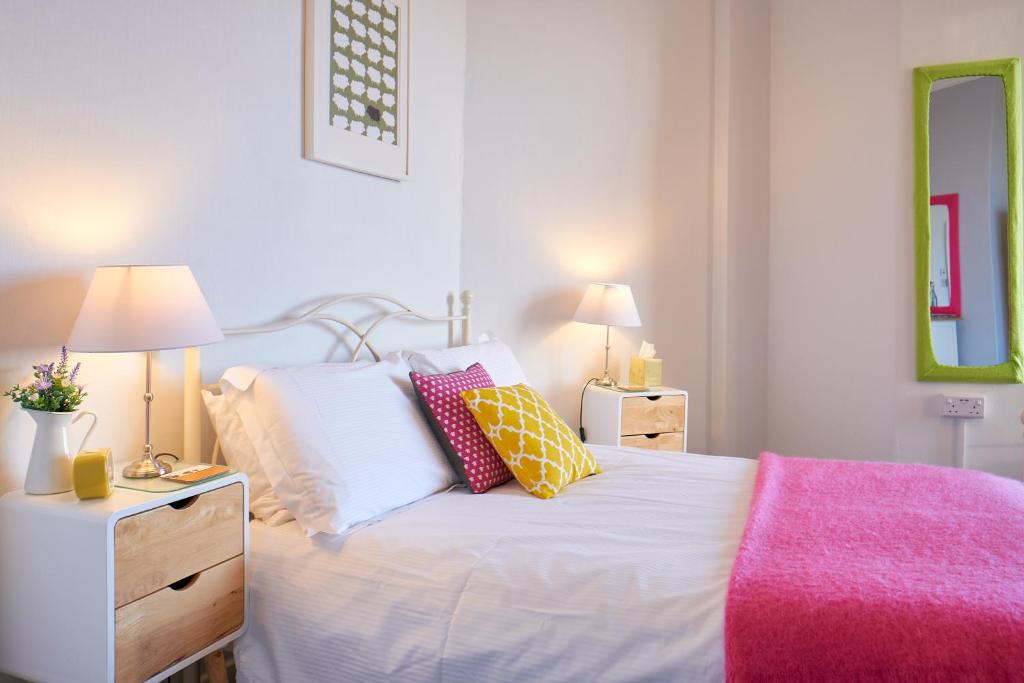 a bedroom with a white bed with pillows and a pink blanket at Corner Beech House in Grange Over Sands