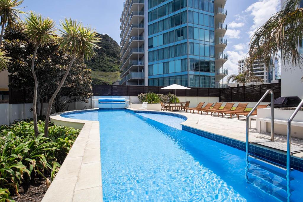 a swimming pool with chairs and a building at Capri on Pilot Bay in Mount Maunganui