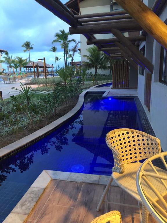 uma piscina de resort com uma cadeira e uma mesa em Apartamento Polinésia - Porto de Galinhas em Porto de Galinhas