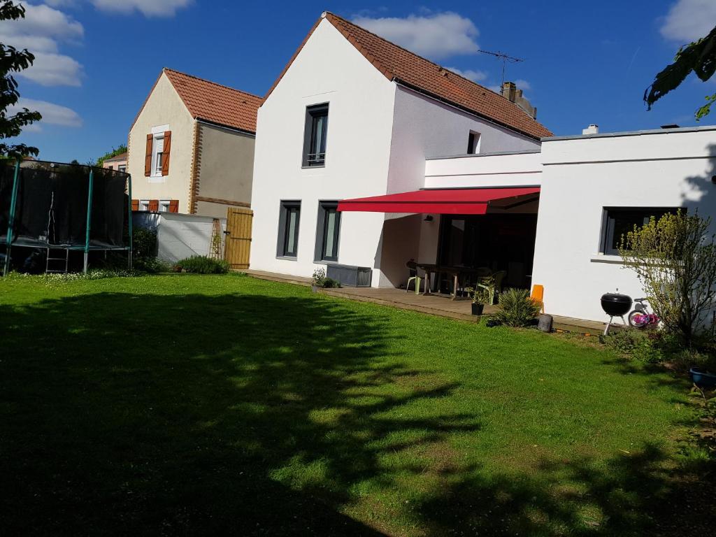 a white house with a red awning and a yard at Chambres privées proche DISNEY Parcs in Chanteloup-en-Brie