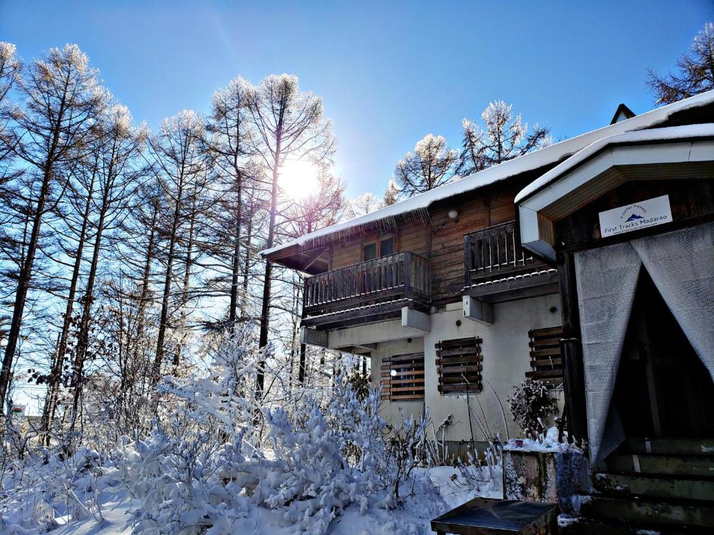 un edificio con nieve en el suelo junto a los árboles en First Tracks Madarao en Iiyama