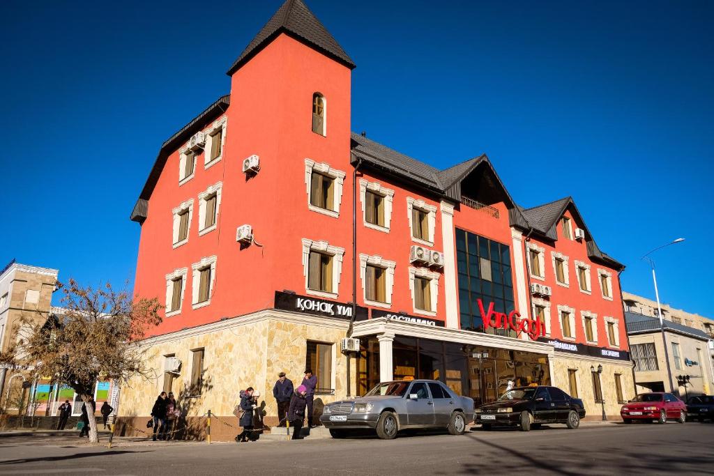 un grand bâtiment rouge dans une rue avec des voitures garées devant dans l'établissement Hotel Vangogh, à Kyzylorda