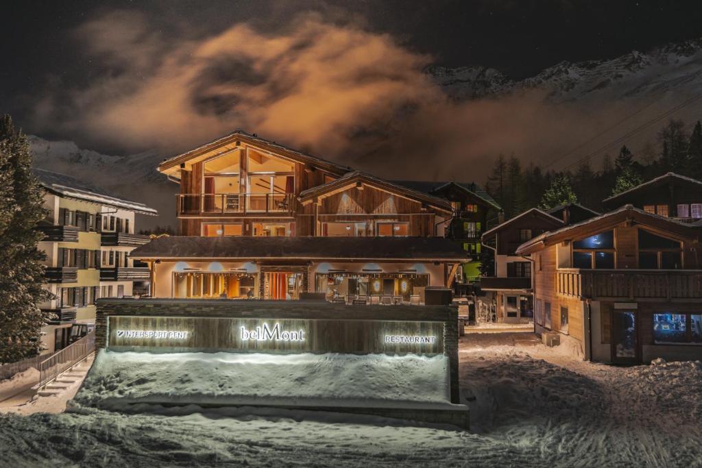 a large wooden house in the snow at night at Apart Lodge belMont in Saas-Fee
