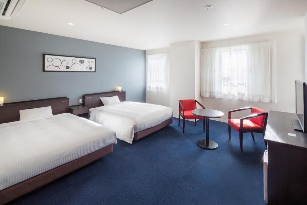 a hotel room with two beds and a table and chairs at Hotel Mystays Nayoro in Nayoro