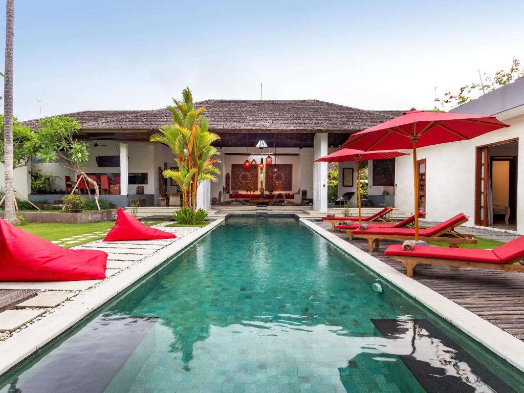 a pool with chairs and umbrellas in front of a house at Villa Arte in Seminyak