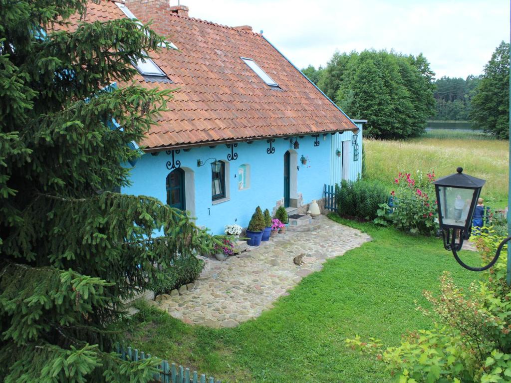 a blue house with a red roof in a yard at Pod tulipanem nad jeziorem in Zawady Oleckie