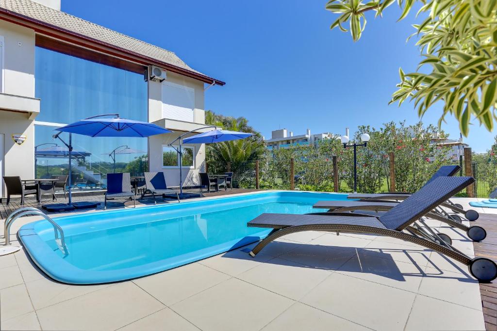 a pool with chairs and umbrellas next to a house at Pousada Ilha Faceira in Florianópolis