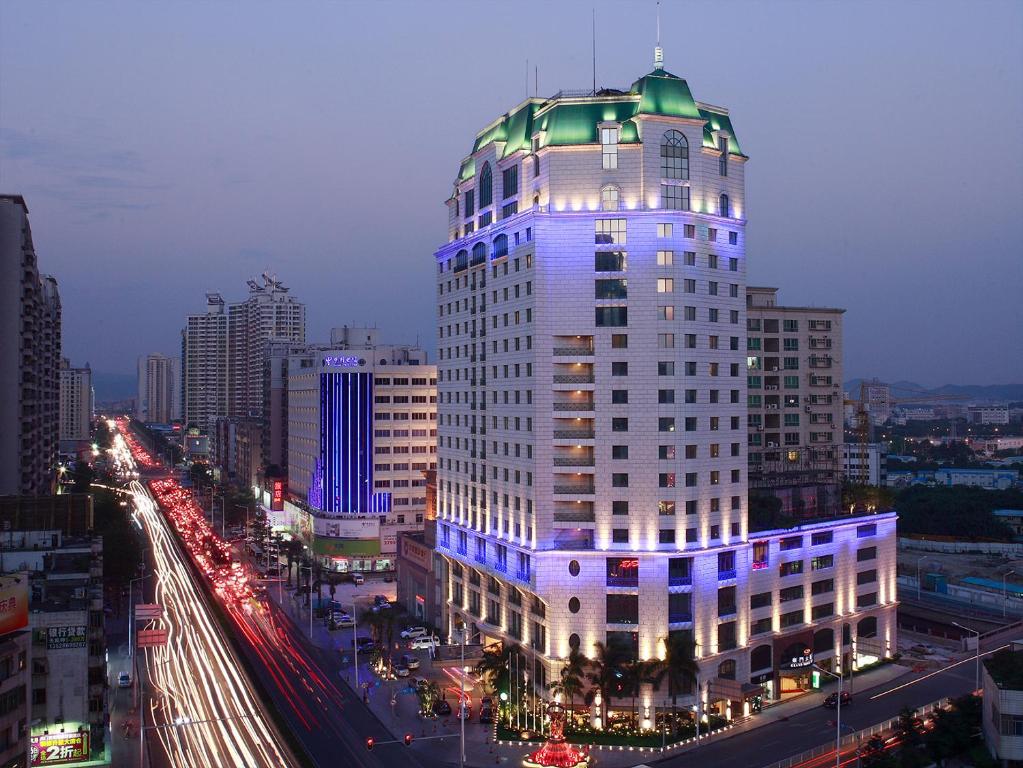 Grand Noble Hotel Dongguan في دونغقوان: مبنى أبيض طويل وبه أضواء زرقاء