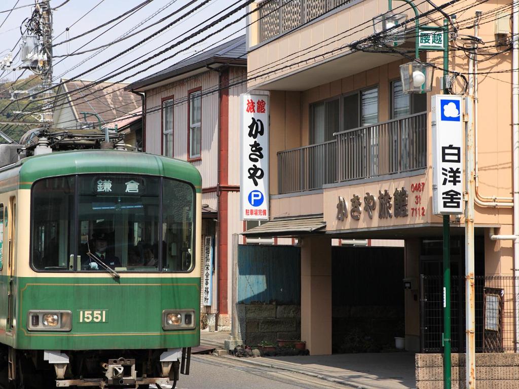 a green train traveling down a street next to a building at Kakiya Ryokan in Kamakura