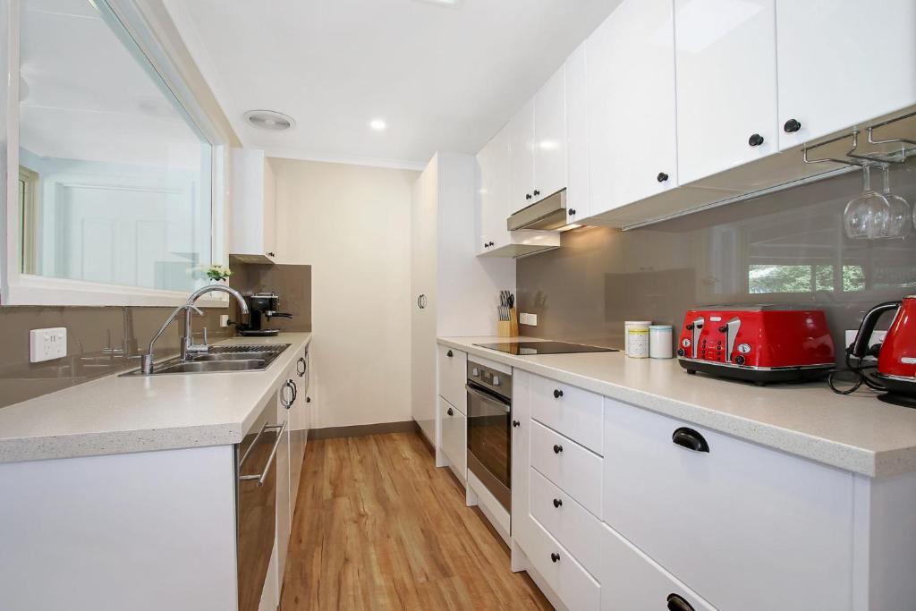 a kitchen with white cabinets and a red appliance at Acaronar in Bright
