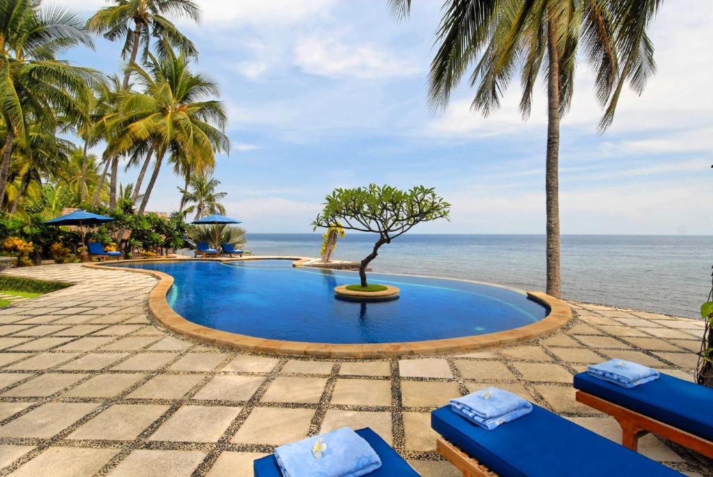 una piscina junto al océano con palmeras en Agung Bali Nirwana Villas and Spa, en Tejakula