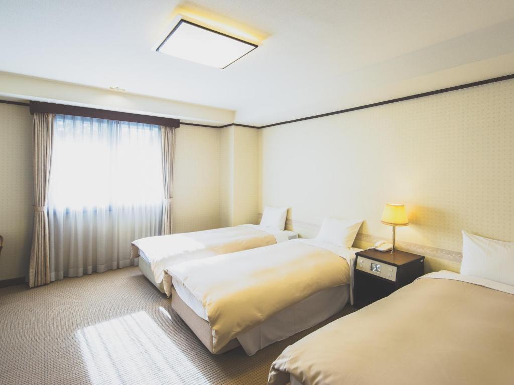 軽井沢町にある ホテル軽井沢エレガンスのベッド3台と窓が備わるホテルルームです。