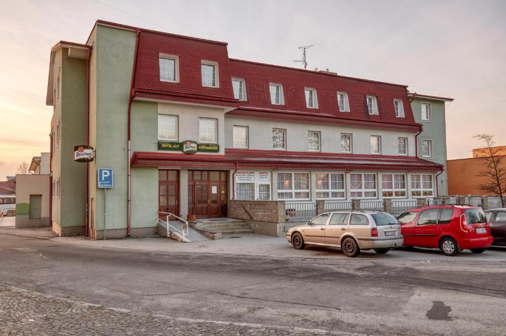 Borovany的住宿－Hotel Alf，两辆车停在大楼前的建筑物