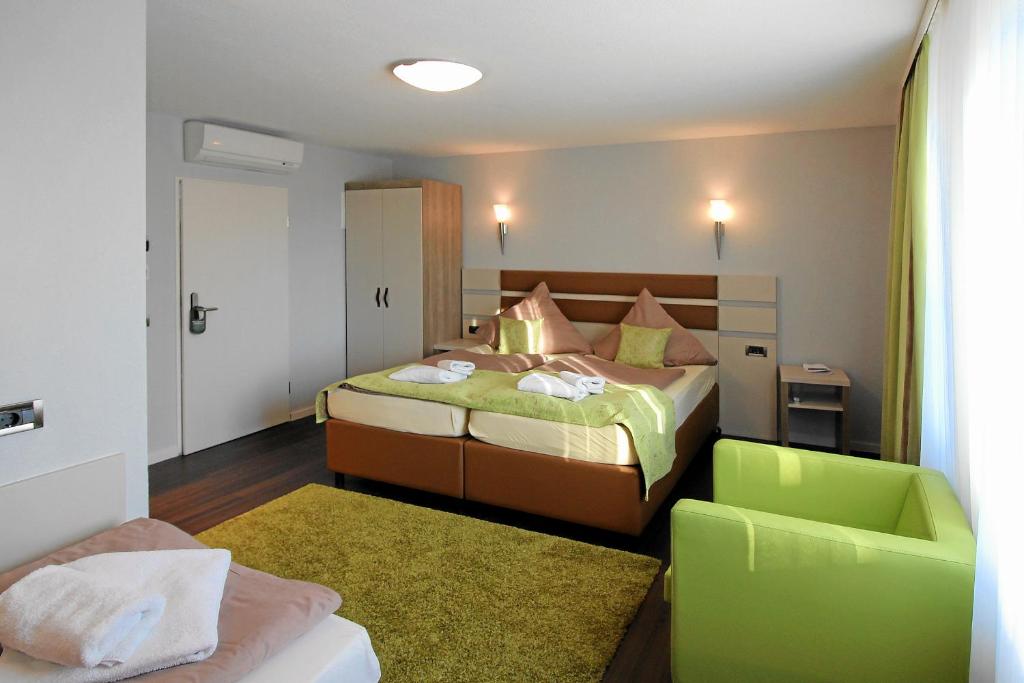 a bedroom with a bed and a green chair at Hotel-Restaurant Axion in Weil am Rhein