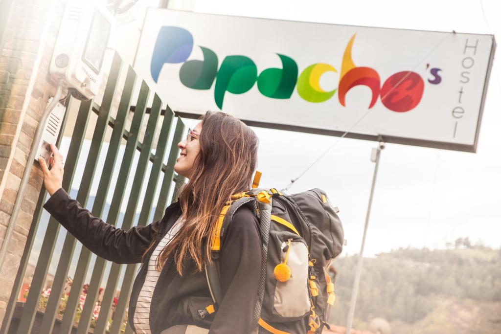 a woman with a backpack standing in front of a sign at Papachos Hostel in Baños