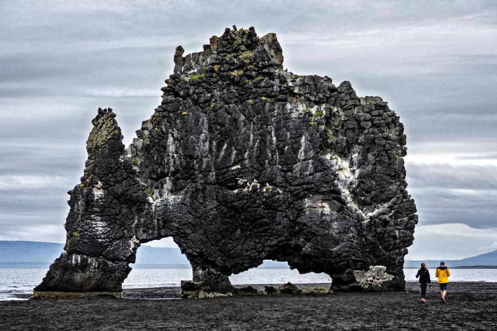 two people standing in front of a rock formation on the beach at Ósar Hostel in Tjörn