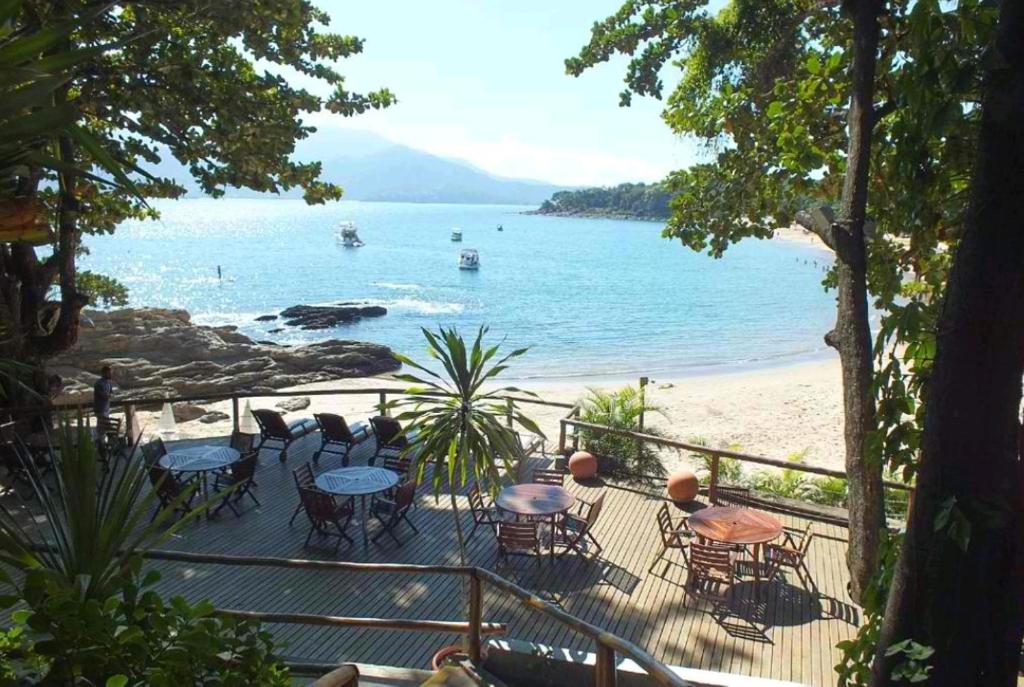 un balcón con mesas y sillas en una playa en Bangalô com vista para o mar no condomínio Yacamim Ilhabela praia do Curral, en Ilhabela