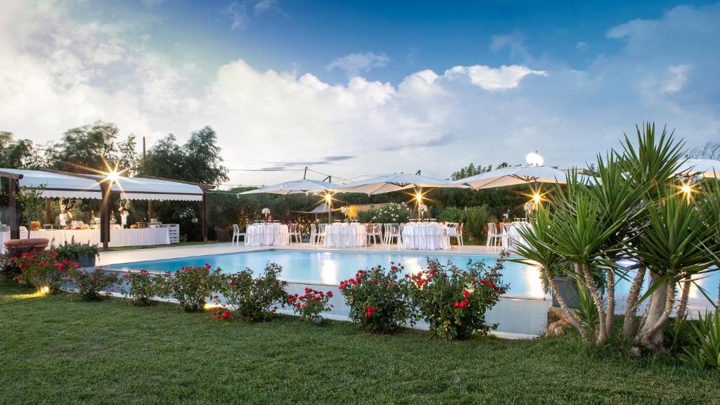 a swimming pool with flowers and tables and umbrellas at Agriturismo Torre Flavia in Ladispoli