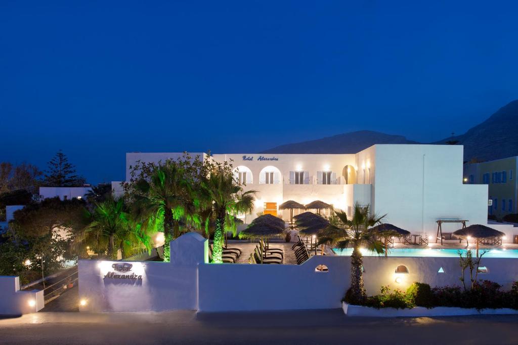 a large white building with palm trees at night at Alexandra Hotel in Kamari