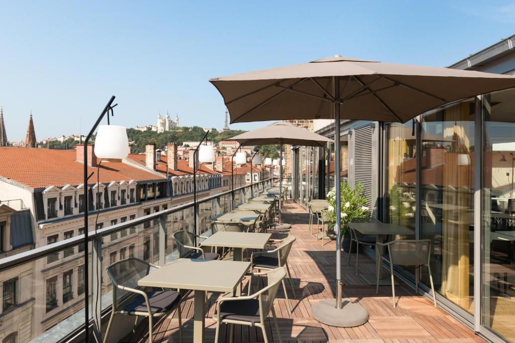 a balcony with tables and chairs and an umbrella at Maison Nô - Hôtel et Rooftop in Lyon