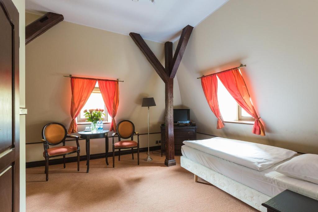 a bedroom with a bed and a table and two windows at Hotel Fryderyk in Duszniki Zdrój