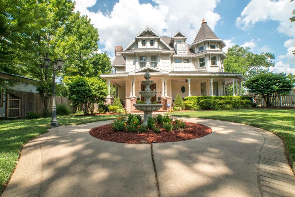 une grande maison blanche avec une fontaine dans l'allée. dans l'établissement The Victoria Bed & Breakfast, à Bentonville