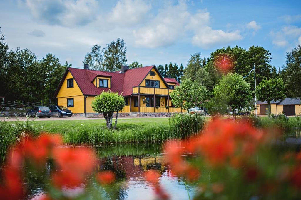 a yellow house with a red roof next to a pond at Pusi Holiday House in Pusi