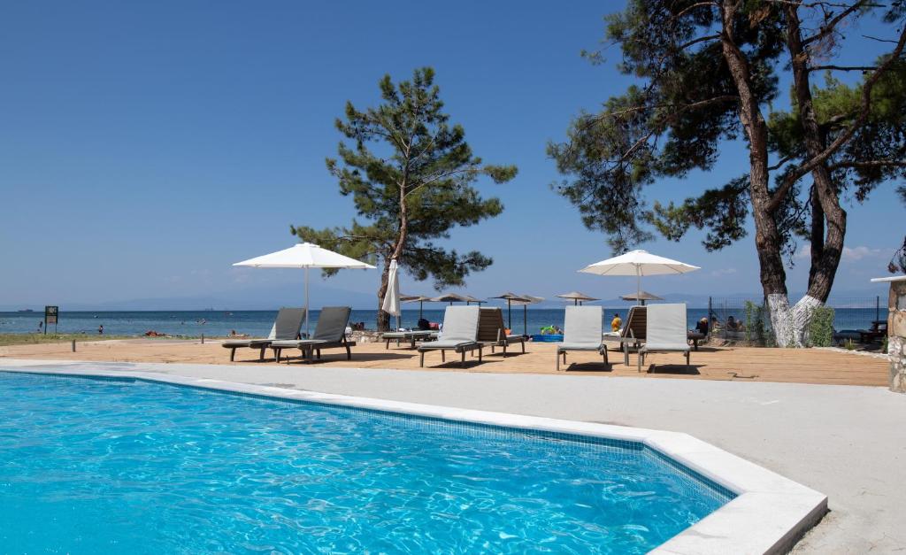 a swimming pool next to a beach with chairs and umbrellas at Rachoni Imperial in Skala Rachoniou