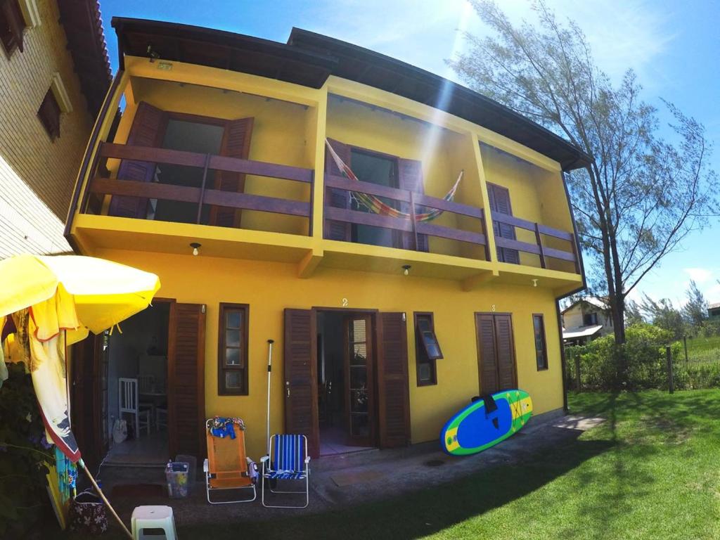 a yellow house with chairs and an umbrella at Residencial Sol de Ibiraquera in Barra de Ibiraquera