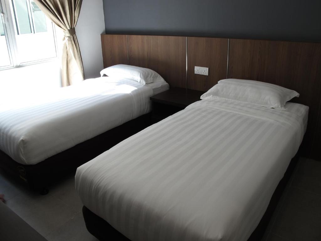 two beds in a hotel room with a window at HOTEL SUKARAMAI in Kampung Gurun