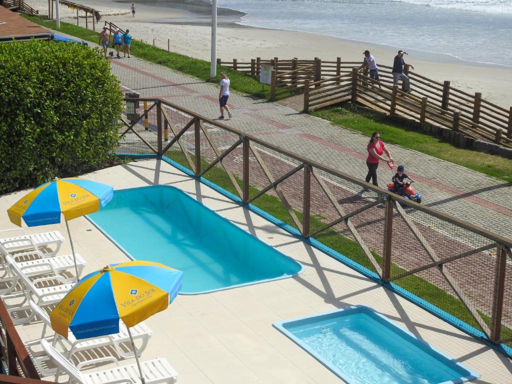 una vista aérea de 2 piscinas y sombrillas junto a una playa en Residencial Vila do Sol, Apartamentos com pé na areia, en Bombinhas