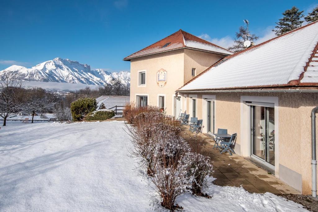 a house in the snow with mountains in the background at "La Combe Fleurie" Appartements & Chambres in Saint-Bonnet-en-Champsaur