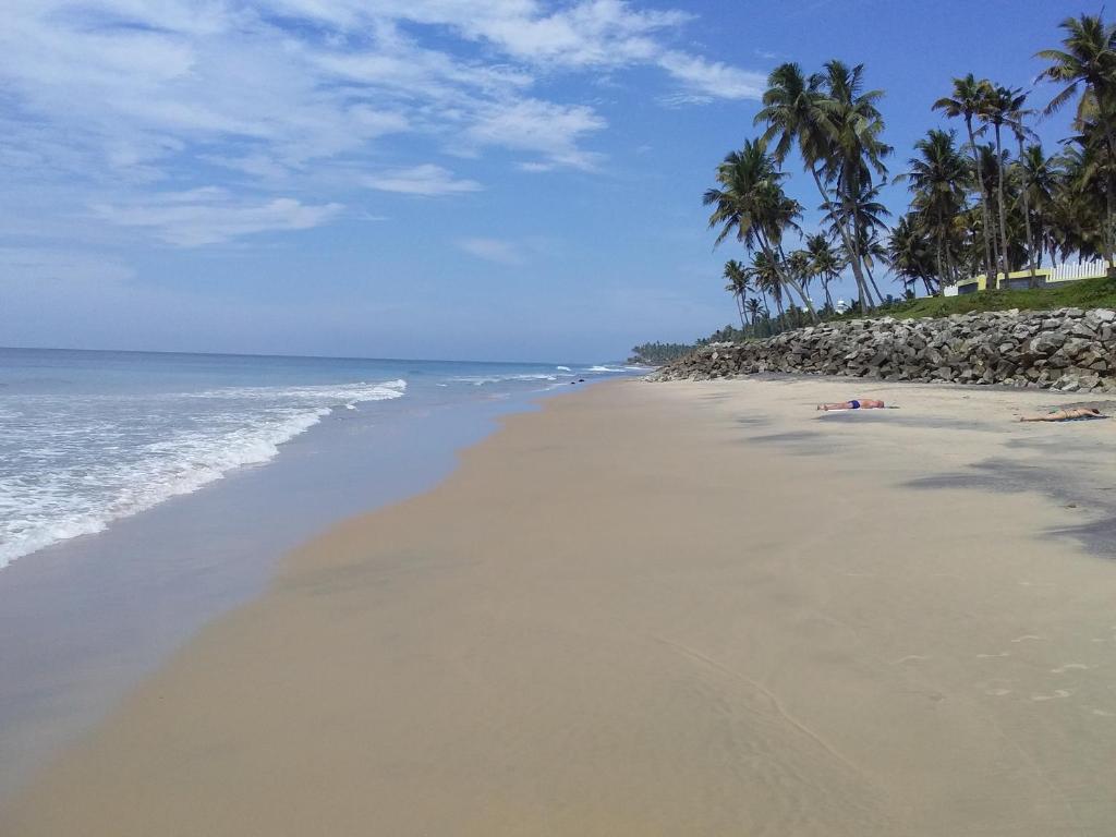 a sandy beach with palm trees and the ocean at The First Place Yogaresort, Odayam in Varkala