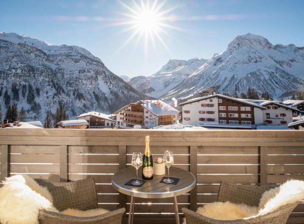 a balcony with a table and chairs and mountains at Hotel Bergkristall Oberlech in Lech am Arlberg