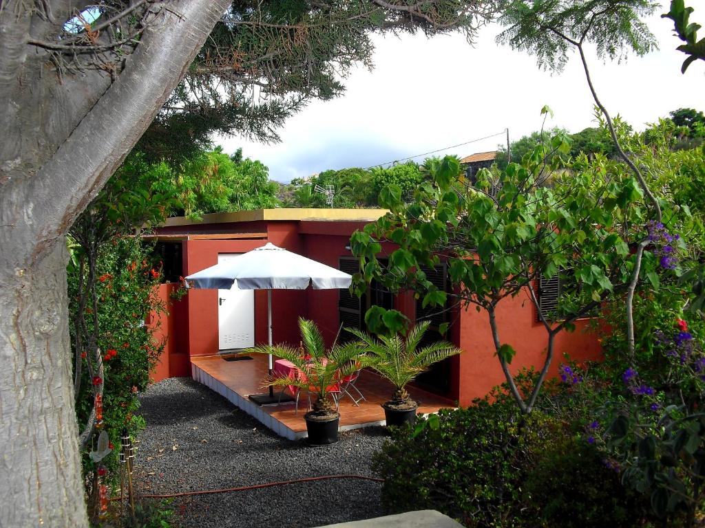 uma casa vermelha com um guarda-chuva branco e algumas plantas em Casa Sandra en Las Norias Todoque con Wi-Fi em Los Llanos de Aridane