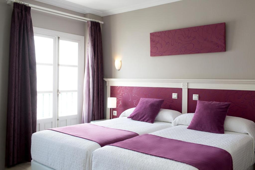two beds in a room with purple and white at Hotel Plaza Cavana in Nerja