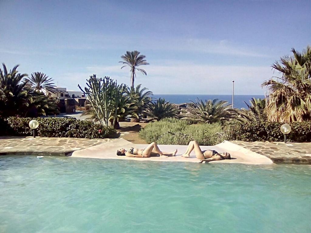 two women laying on a blanket in a swimming pool at Dammuso Villa Giò in Pantelleria