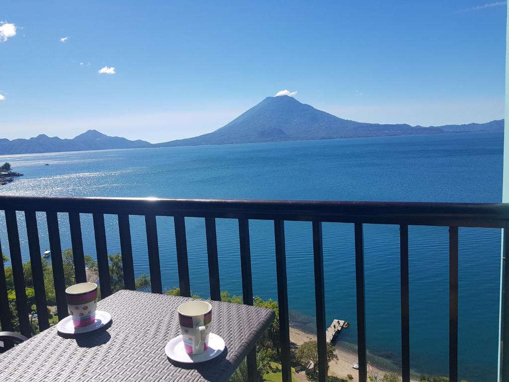 a table with two cups on top of a balcony overlooking the water at Sky view Atitlán lake suites ,una inmejorable vista apto privado dentro del lujoso hotel in Panajachel