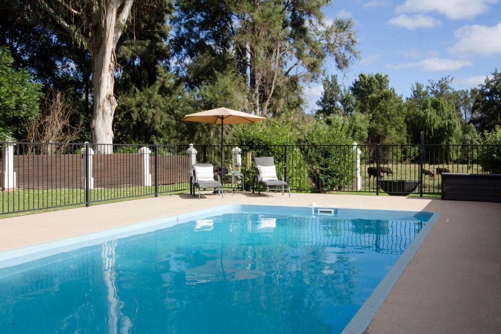 a swimming pool with two chairs and an umbrella at Mudgee Country Grandeur at this Elegant Group Getaway in Mudgee