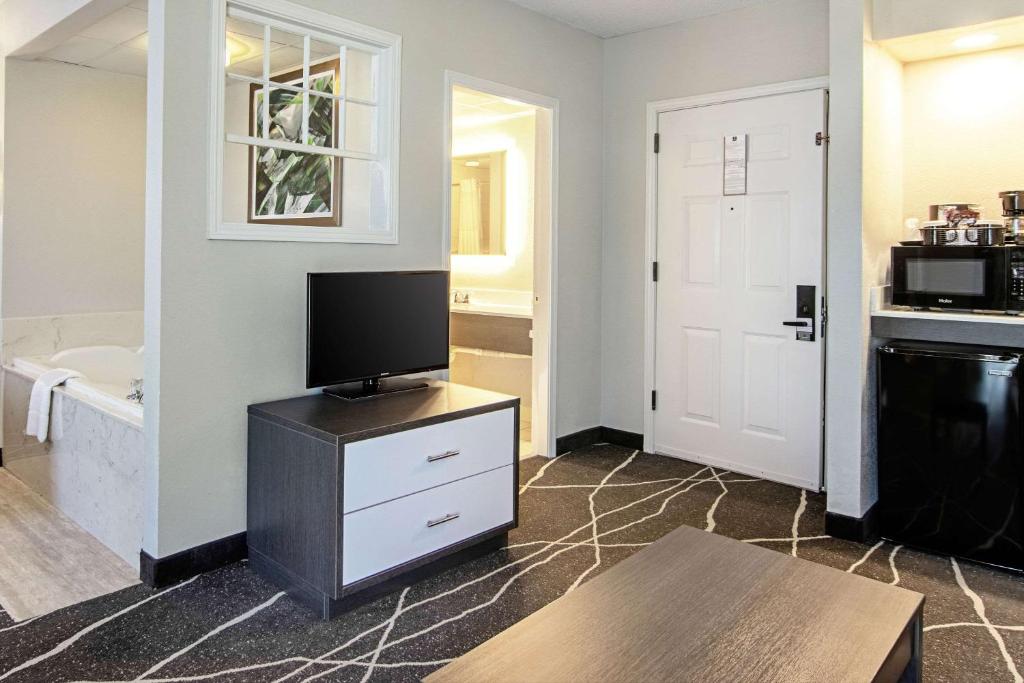 a living room with a tv on a dresser and a bathroom at Clarion Inn Willow River in Sevierville